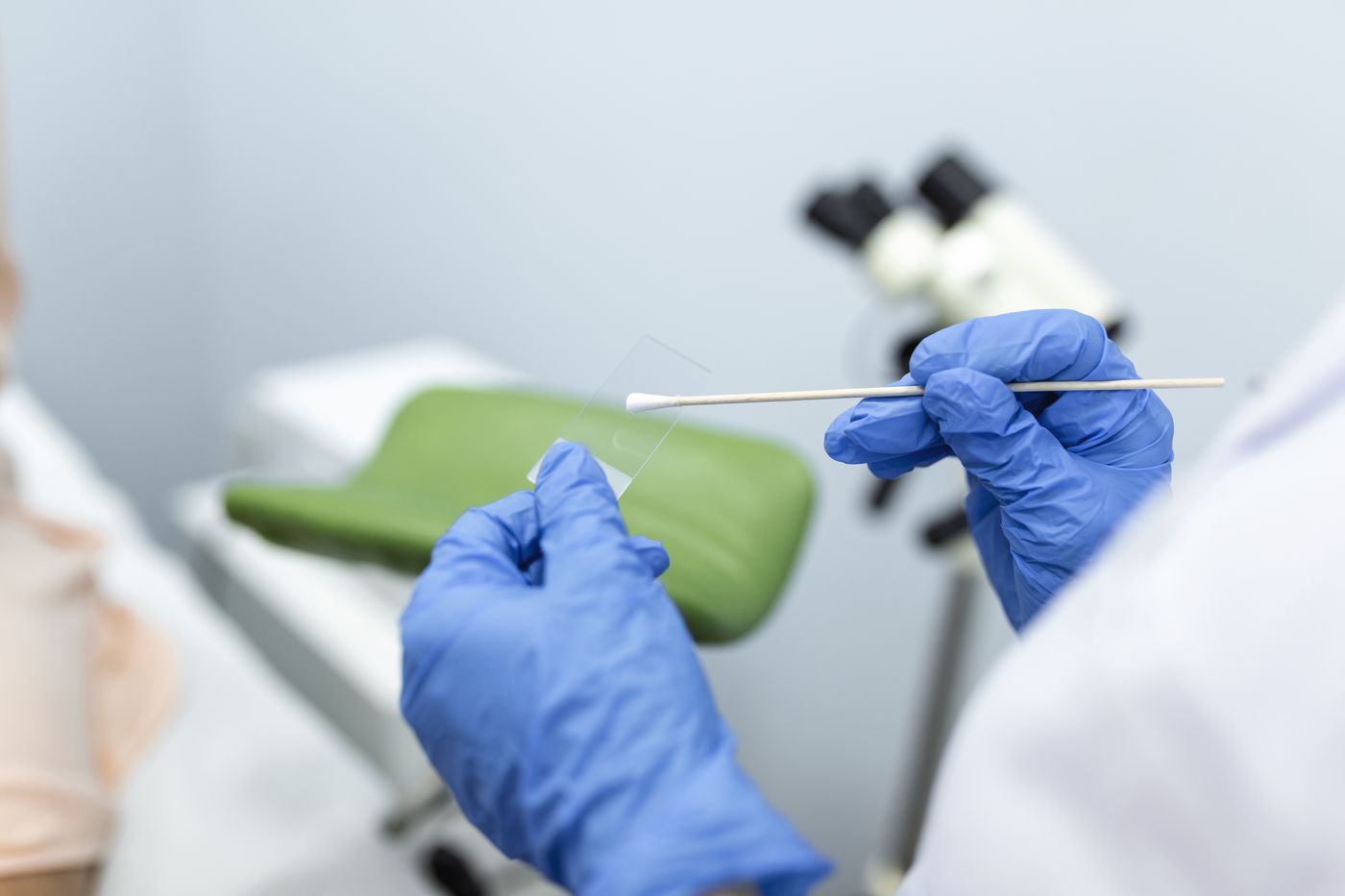 A gloved clinician holding a swab and a glass slide in an examination room