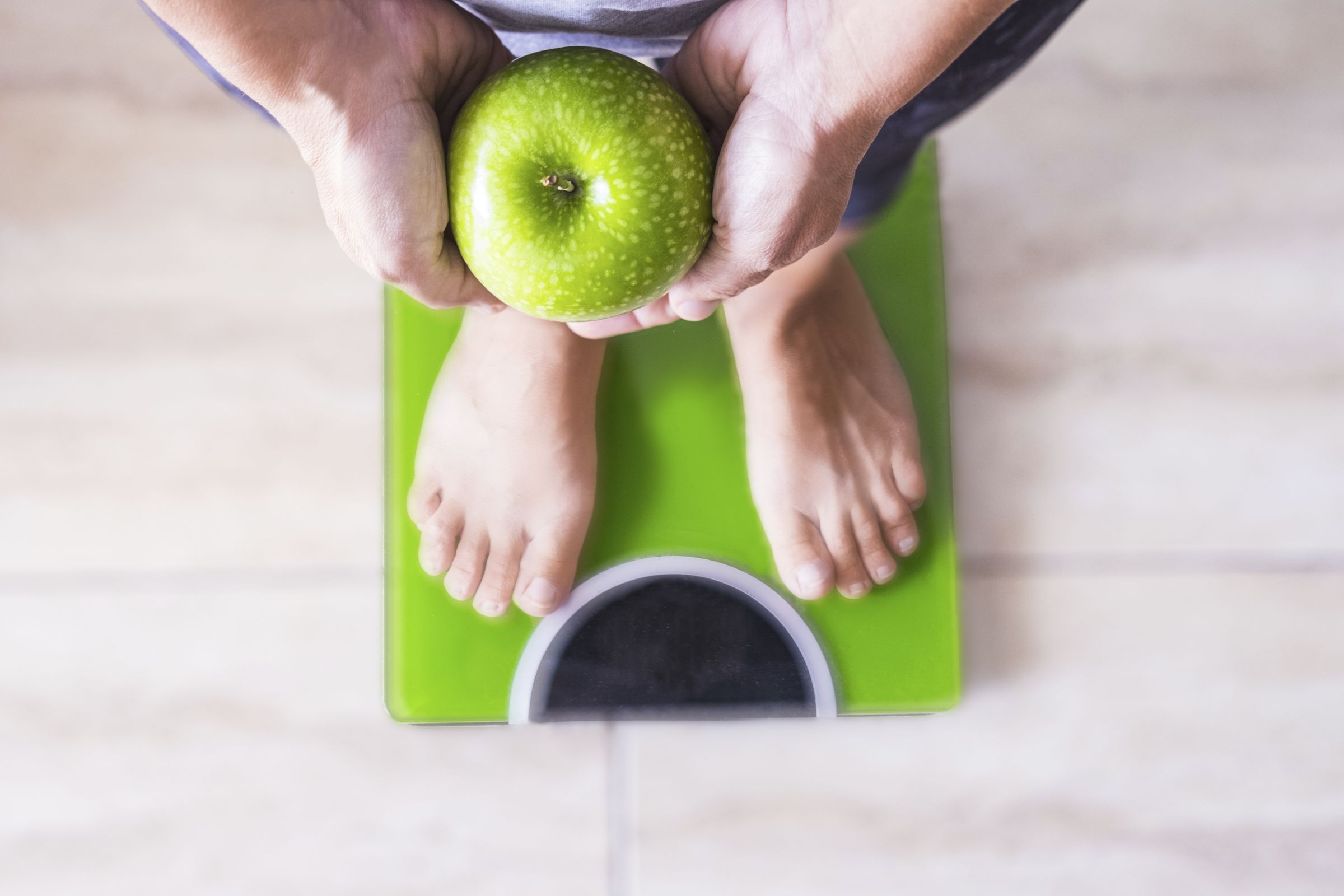 Someone standing on bathroom scales holding a green apple