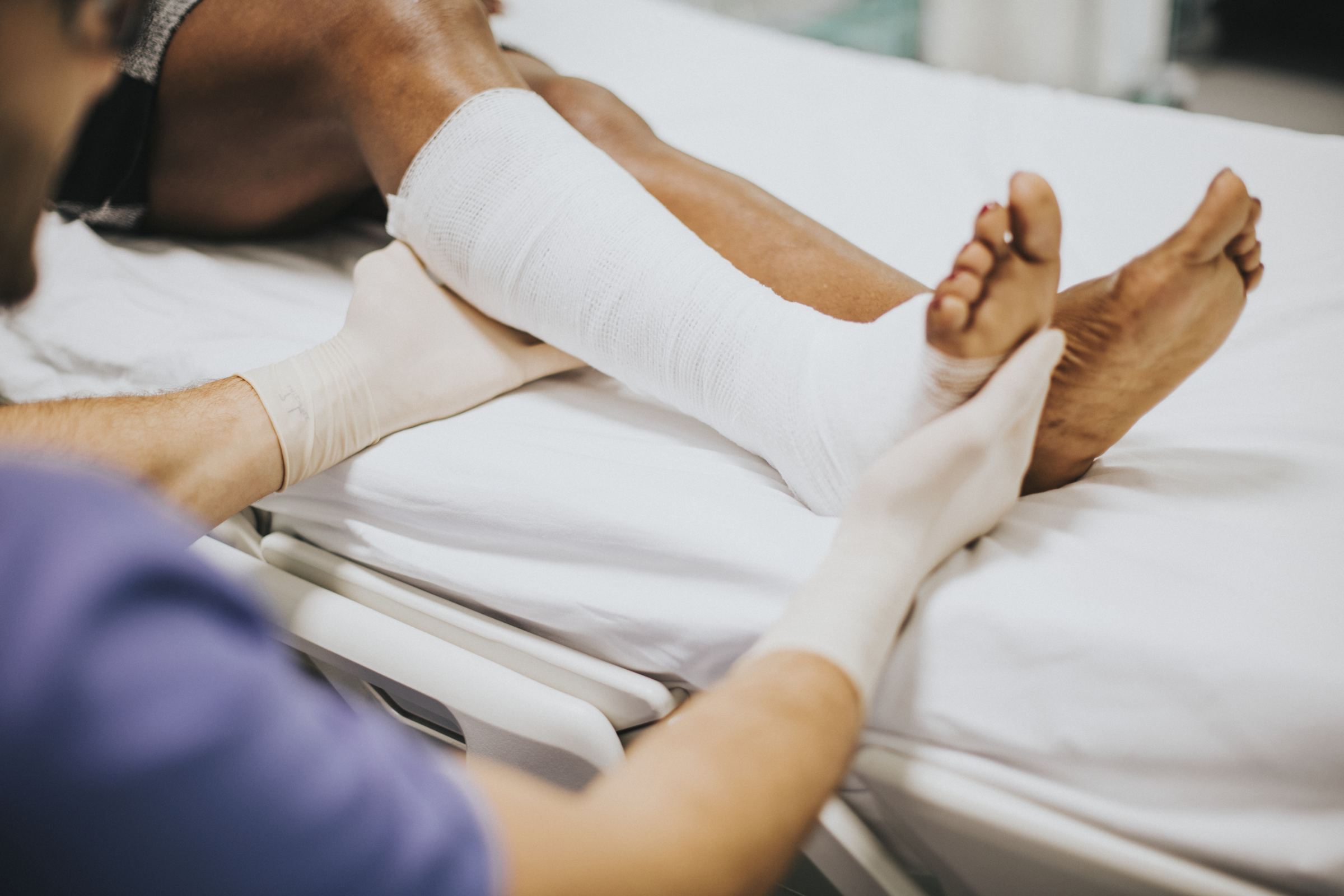 A clinician in gloves supporting a patient's bandaged lower leg